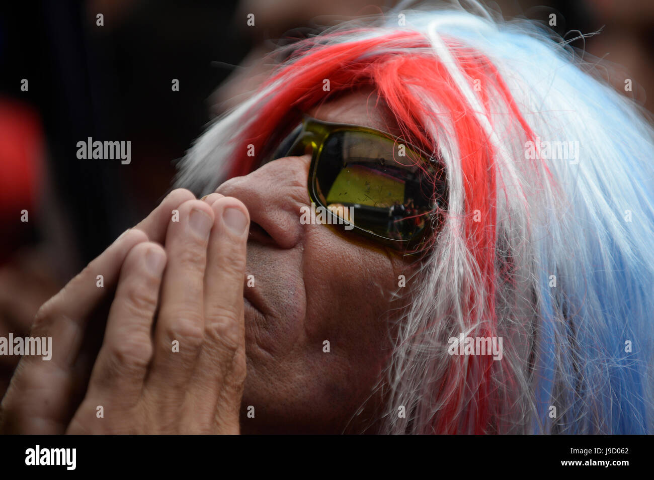 A Costa Rica fan in a wig with the colors of the Costa Rican flag watches in the Plaza de la Democracía in San José as the national team takes on Gree Stock Photo