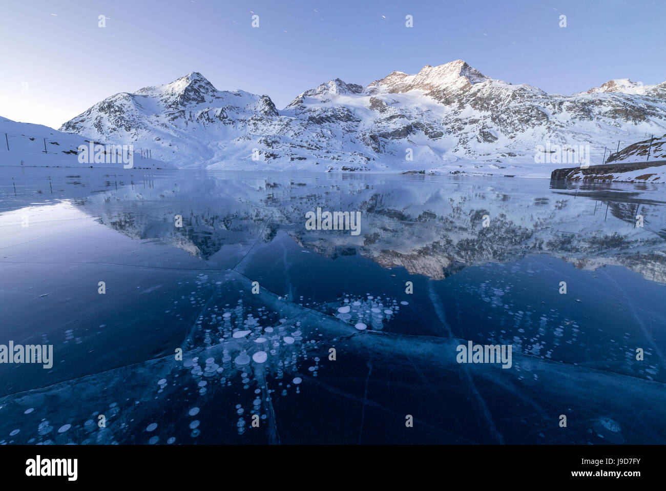 Ice bubbles frame the snowy peaks reflected in Lago Bianco, Bernina Pass, canton of Graubunden, Engadine, Switzerland, Europe Stock Photo