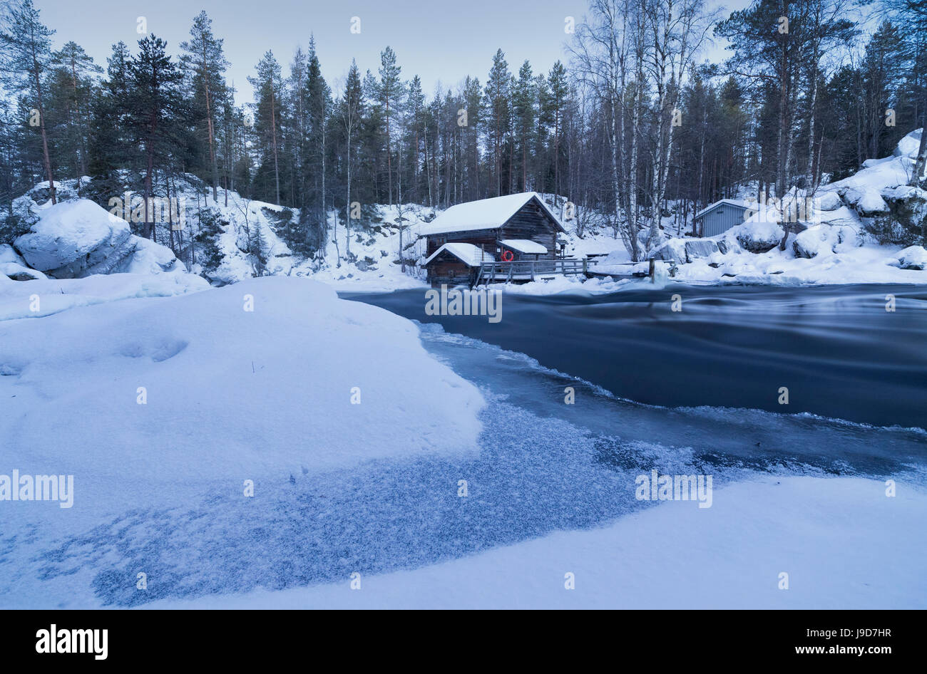 Dusk frames the frozen water in the snowy woods and a wooden hut, Juuma, Myllykoski, Lapland region, Finland, Europe Stock Photo