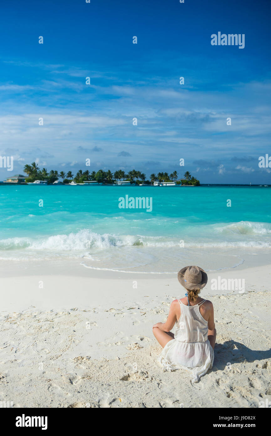 Woman sitting on a white sand beach enjoying the turquoise water, Sun Island Resort, Nalaguraidhoo island, Ari atoll, Maldives Stock Photo