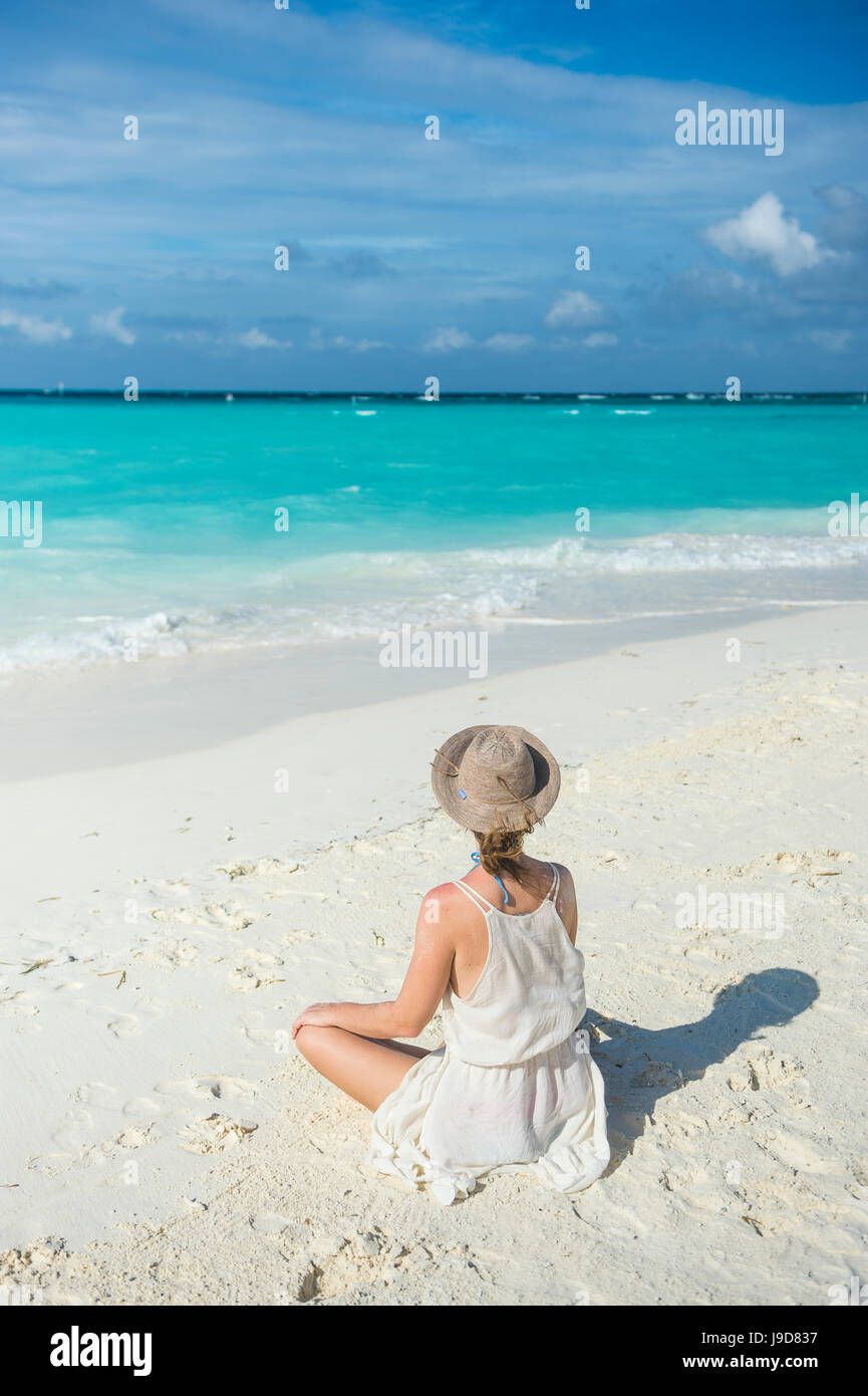 Woman sitting on a white sand beach enjoying the turquoise water, Sun Island Resort, Nalaguraidhoo island, Ari atoll, Maldives Stock Photo