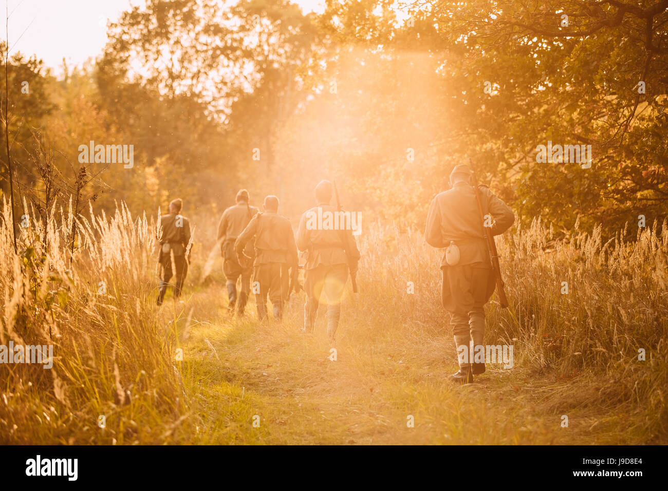Group Of Reenactors Men Dressed As Russian Soviet Red Army Infantry Soldiers Of World War II Marching In Autumn Forest With Weapons At Sunset Time Dur Stock Photo