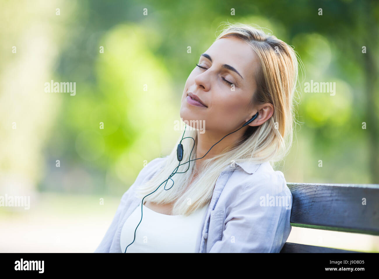 Young happy woman is sitting in park and listening to music Stock Photo ...