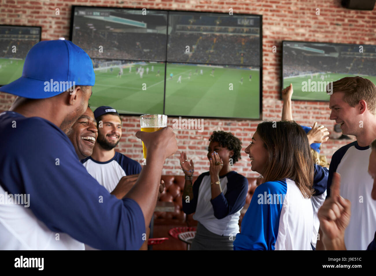 Friends Watching Game In Sports Bar On Screens Celebrating Stock Photo
