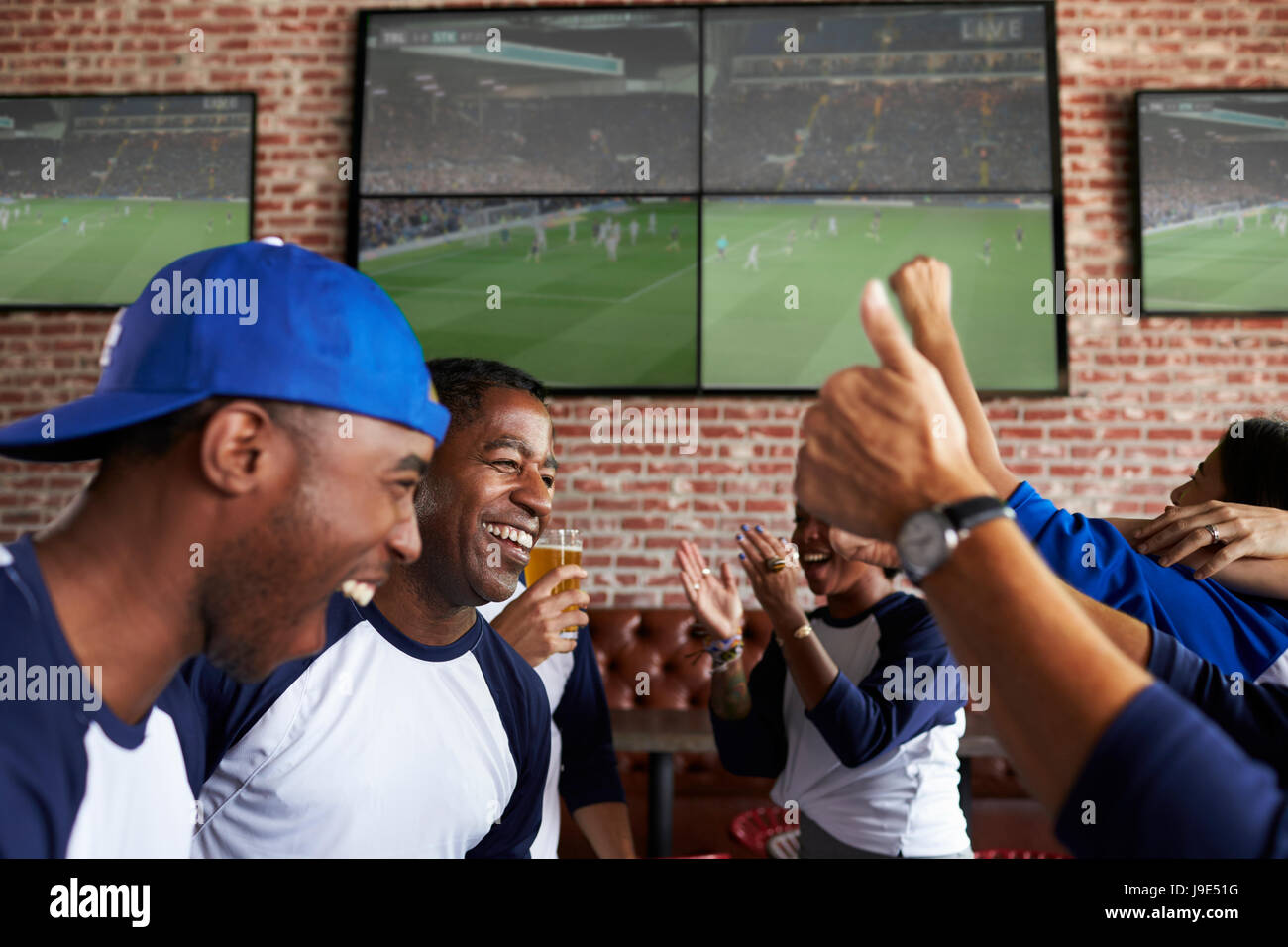 Friends Watching Game In Sports Bar On Screens Celebrating Stock Photo