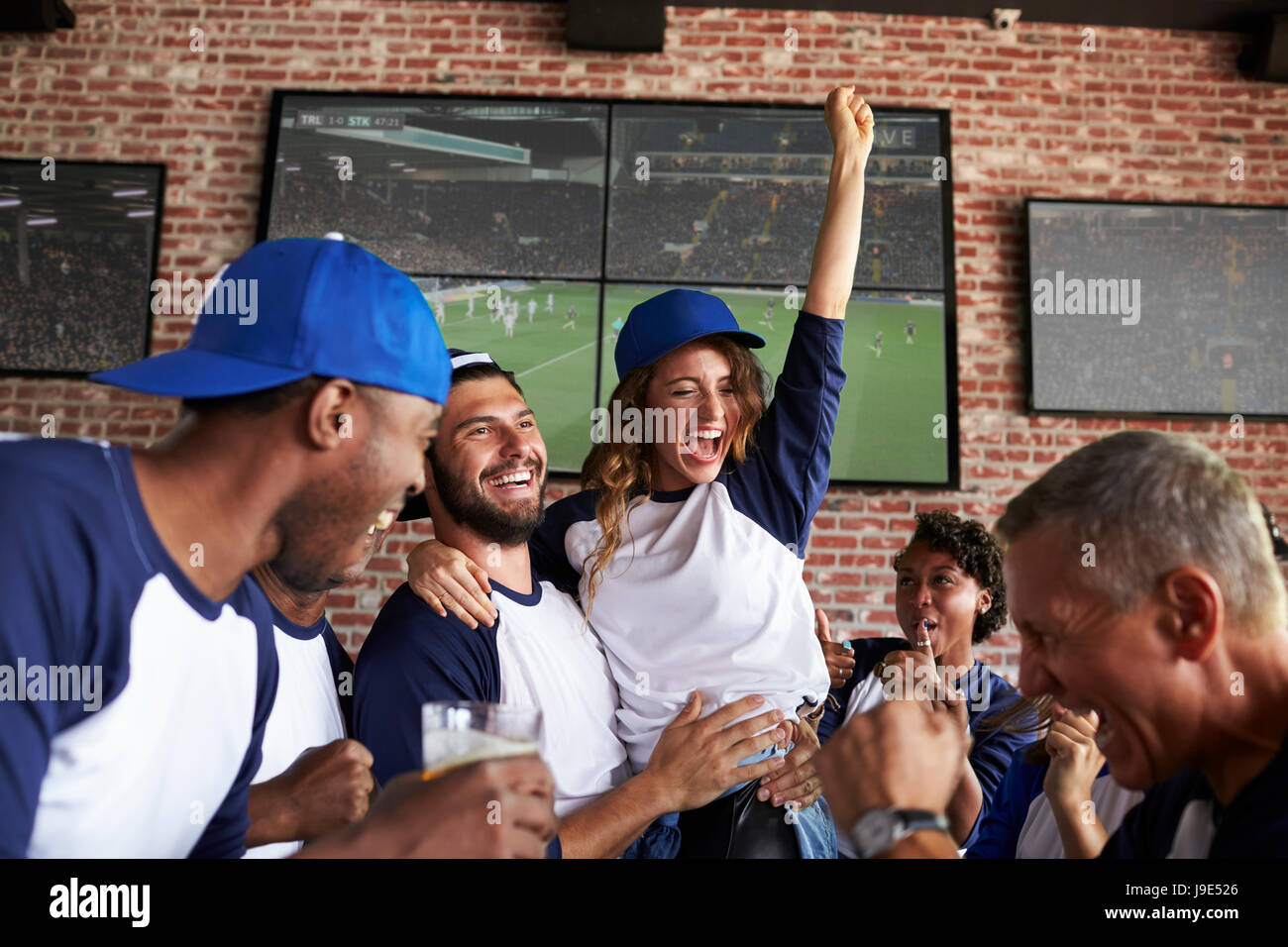 Friends Watching Game In Sports Bar On Screens Celebrating Stock Photo