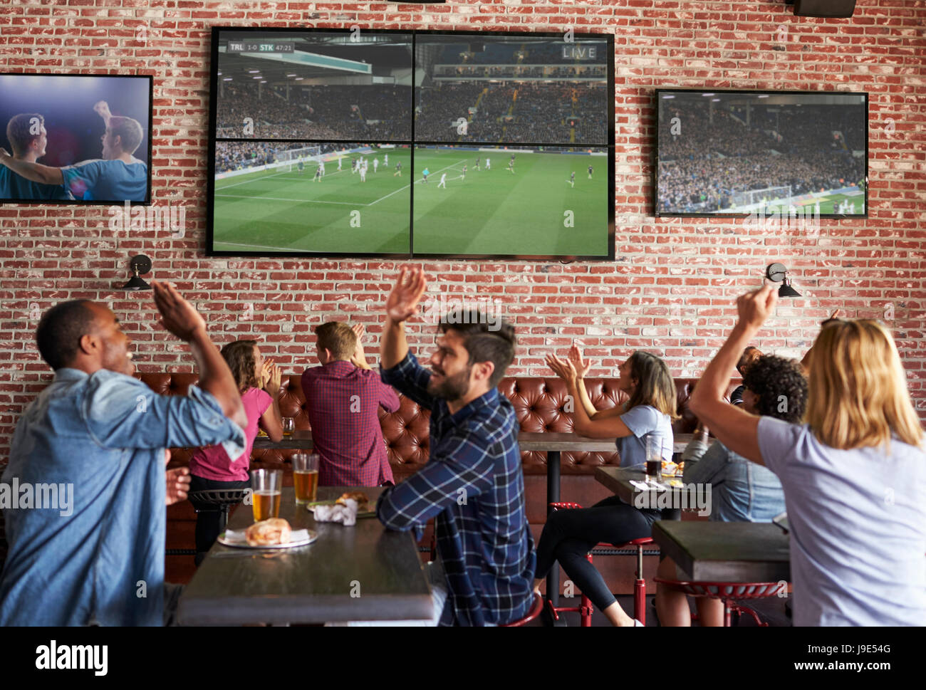 Friends Watching Game In Sports Bar On Screens Celebrating Stock Photo