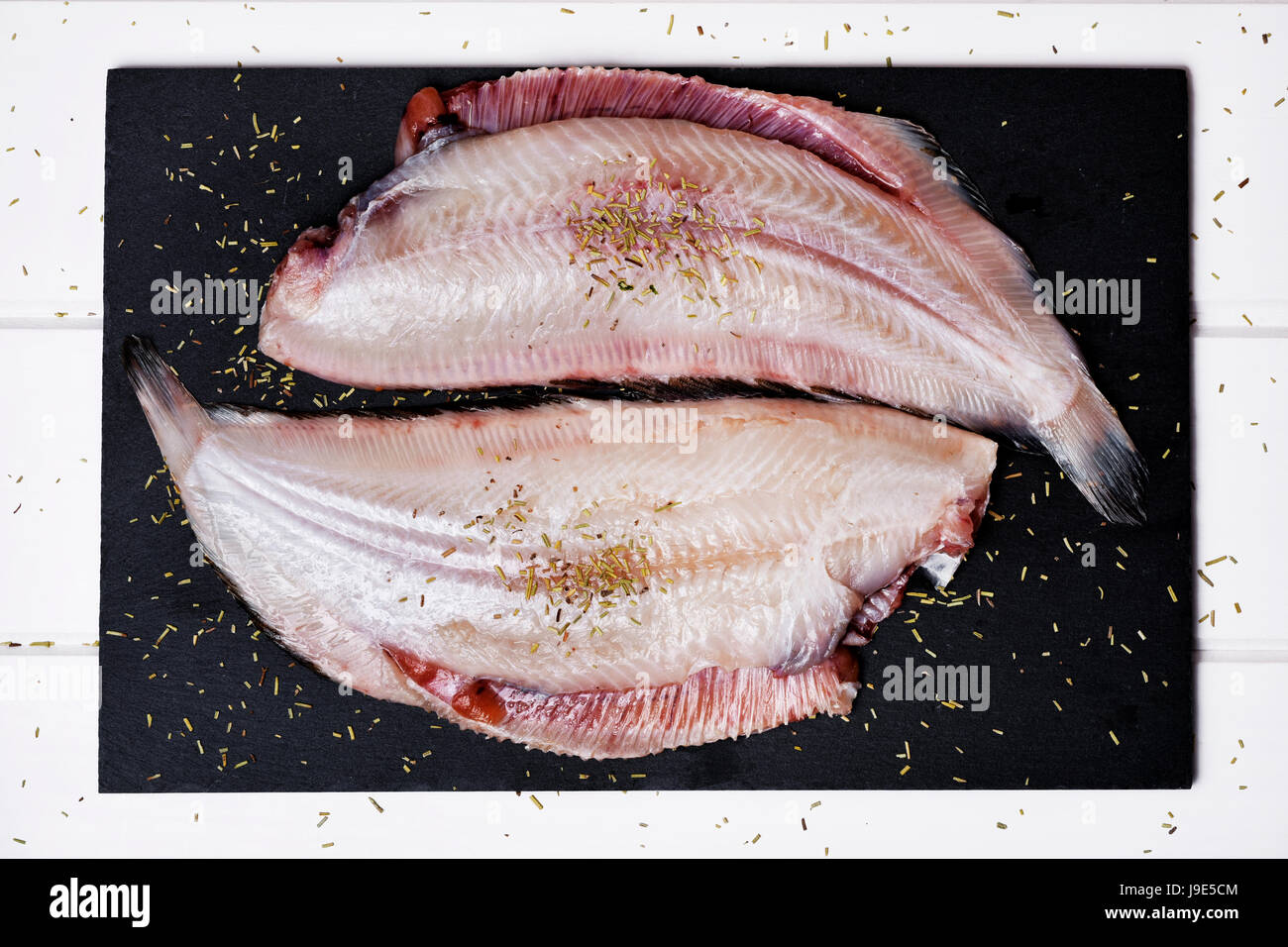 high-angle shot of a pair f raw filleted common sole on a slate tray placed on a rustic wooden table Stock Photo