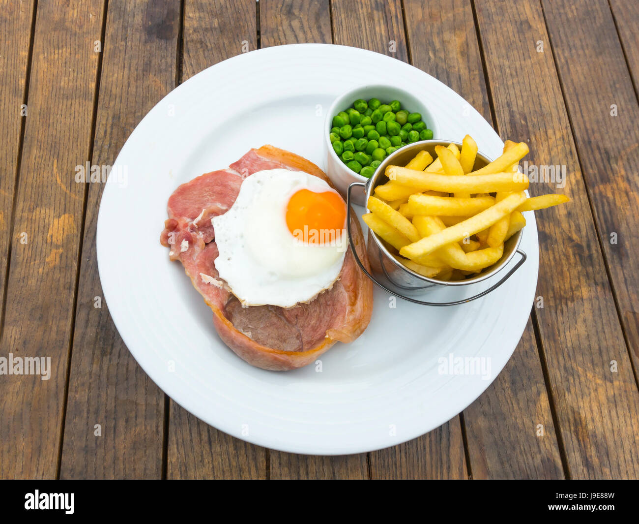 Meal of dry cured gammon rasher fried egg potato chips and peas eaten