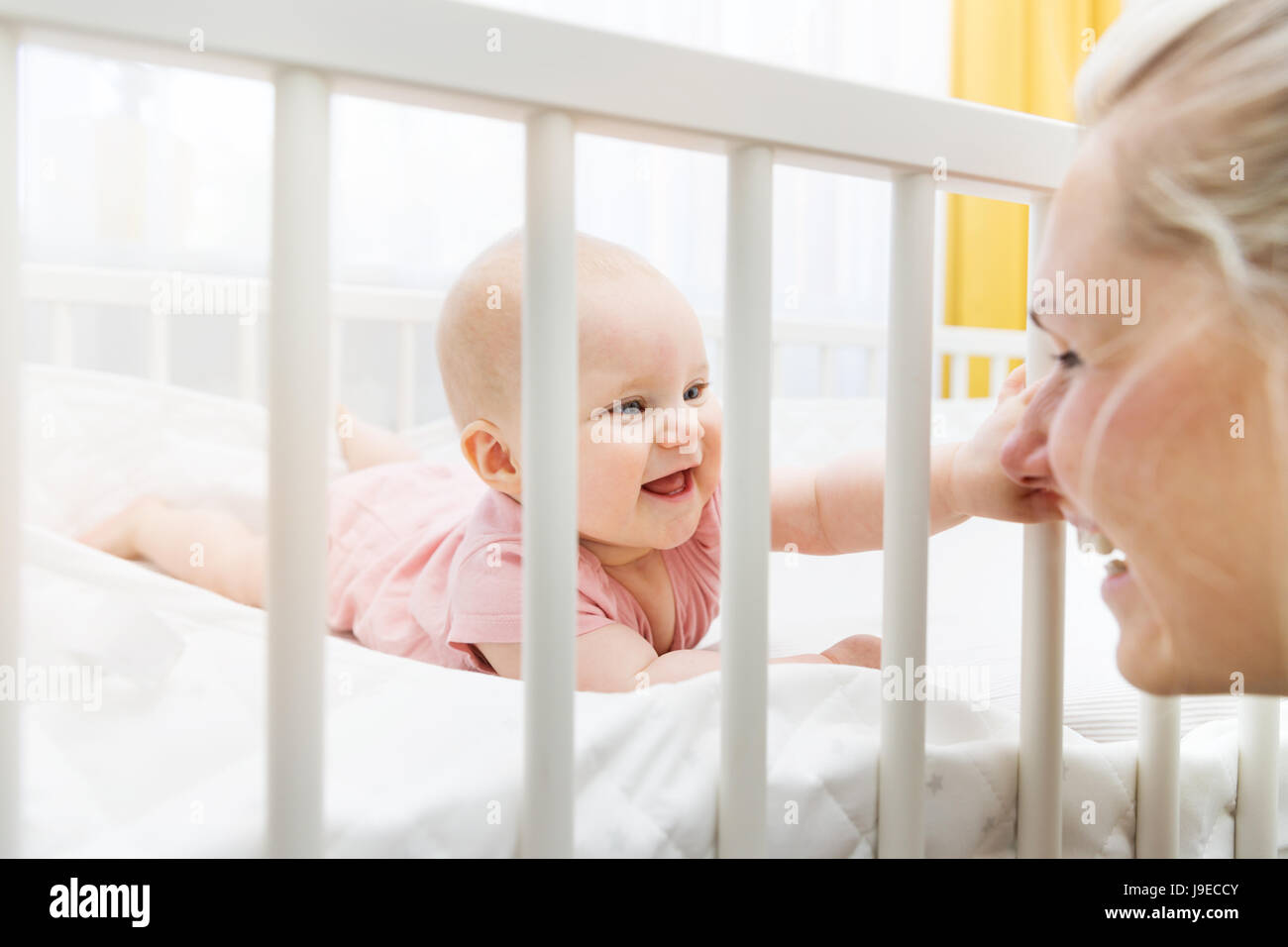 mother playing with her baby in crib and having fun together Stock Photo