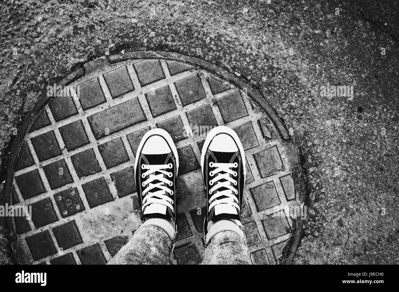 teenager feet in sneakers gumshoes standing an urban manhole cover J9ECH0