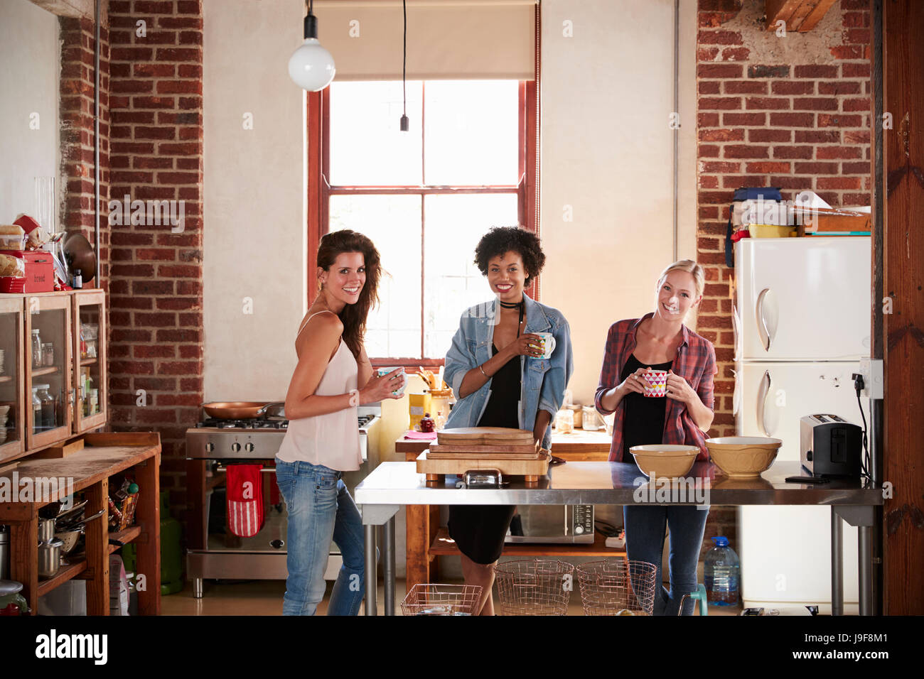 Three young adult girlfriends in kitchen look to camera Stock Photo