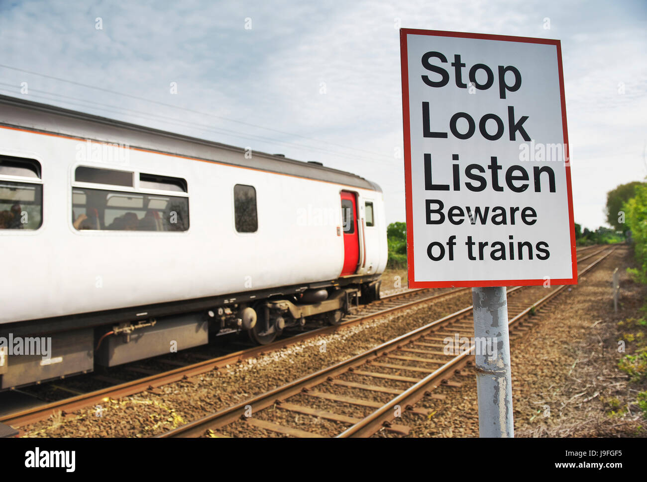 Stop Look Listen Beware of Trains sign on the edge of train tracks in rural norfolk as the diesel train passes Stock Photo