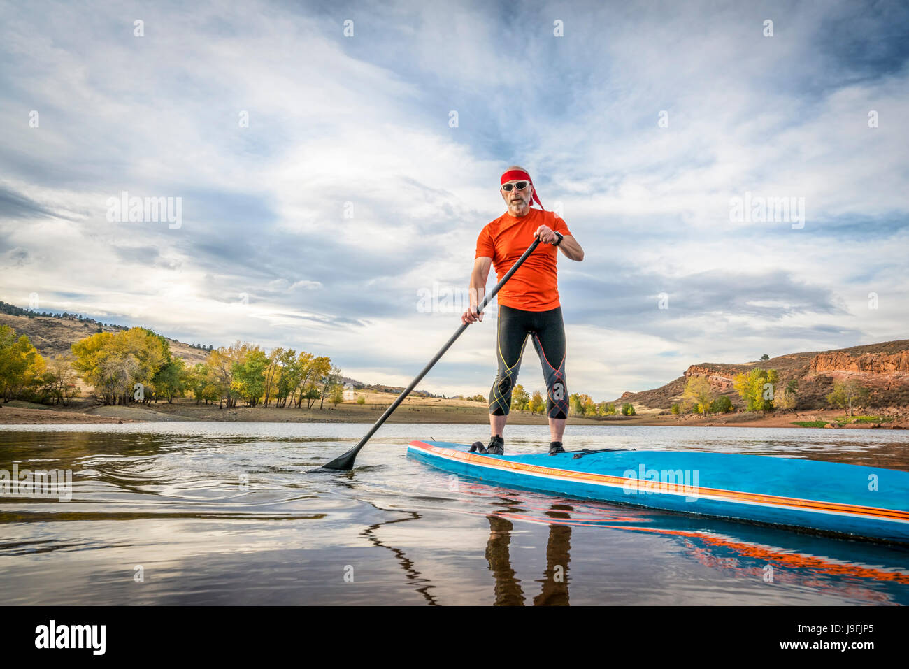 A senior male paddling a stand up paddleboard on a calm mountain lake