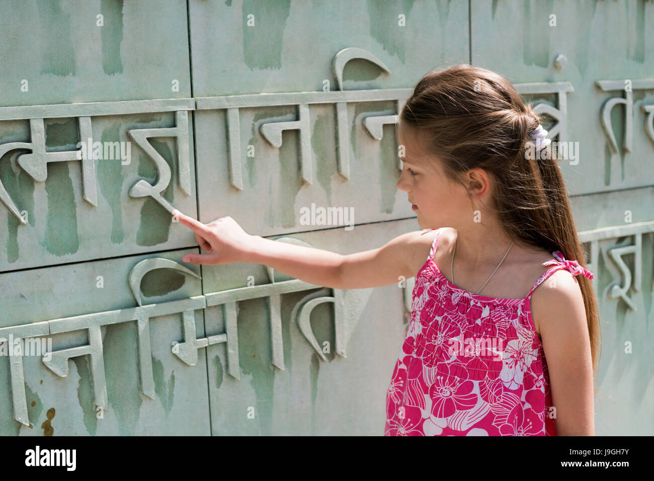 child girl trying to read unknown language letters relief on building wall Stock Photo