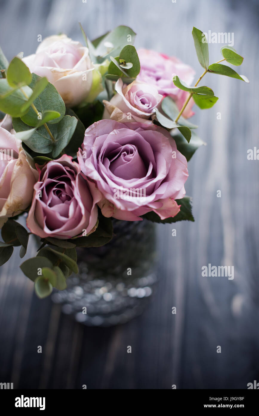 Pastel purple, mauve color fresh summer roses in vase with black tabletop board background, vintage style rustic wedding decor Stock Photo