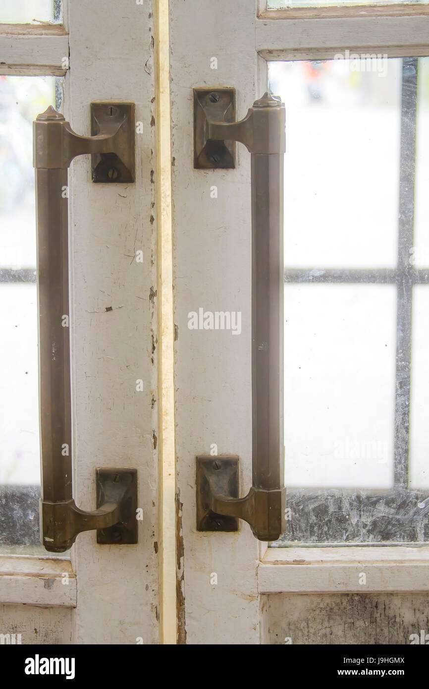 Long metal handles on old wooden doors with chipped white paint and dirty glass panes Stock Photo