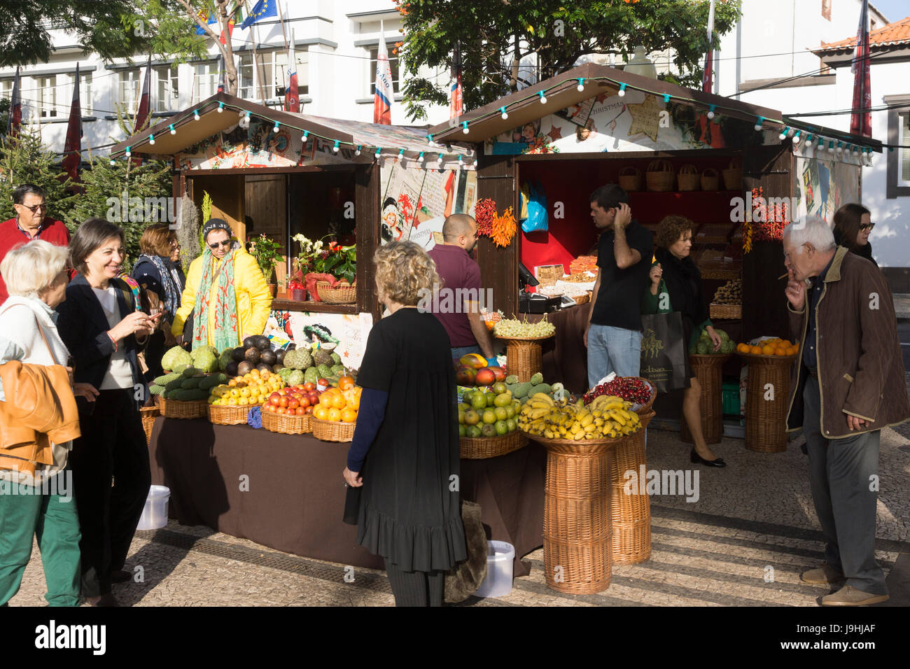 Tourists and locals mingle at a Christmas market in Madeira. Brightly coloured exotic fruits are on sale. Stock Photo