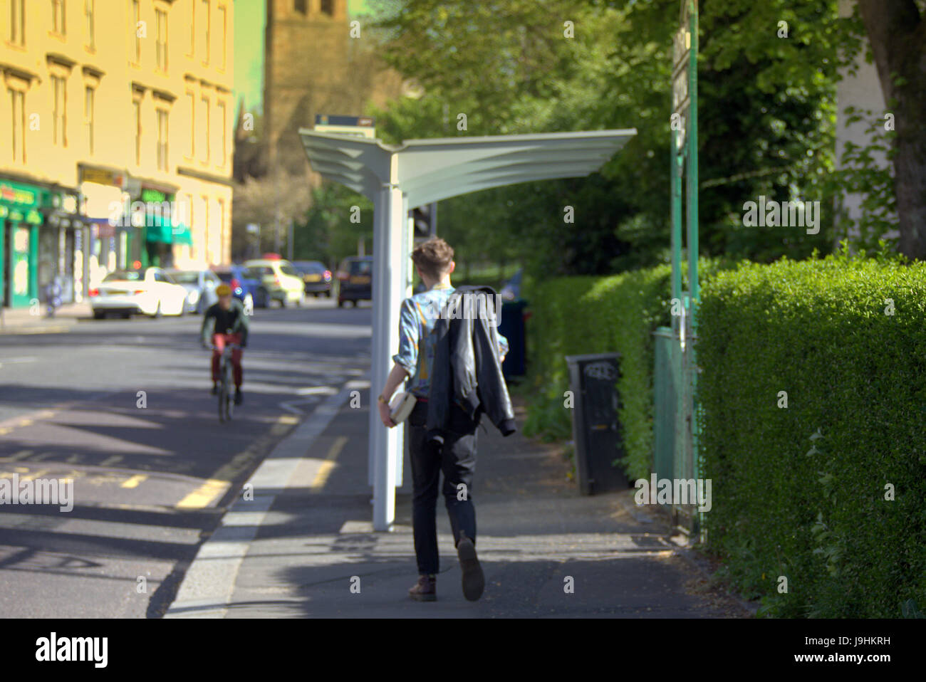 Glasgow street  scene student carrying books at bus stop sunny day park district Stock Photo