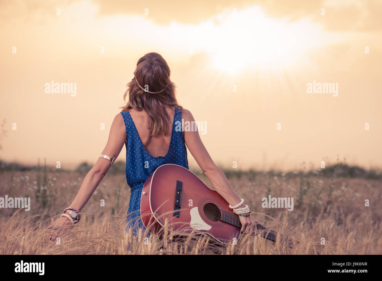Young retro hippy styled woman with acoustic guitar in wheat field looking at sun to find inspiration for the next song. Music, art and lifestyle conc Stock Photo