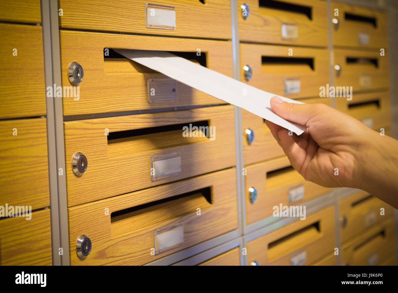 Mailman hand putting the yellow envelope into the gray mailbox Stock