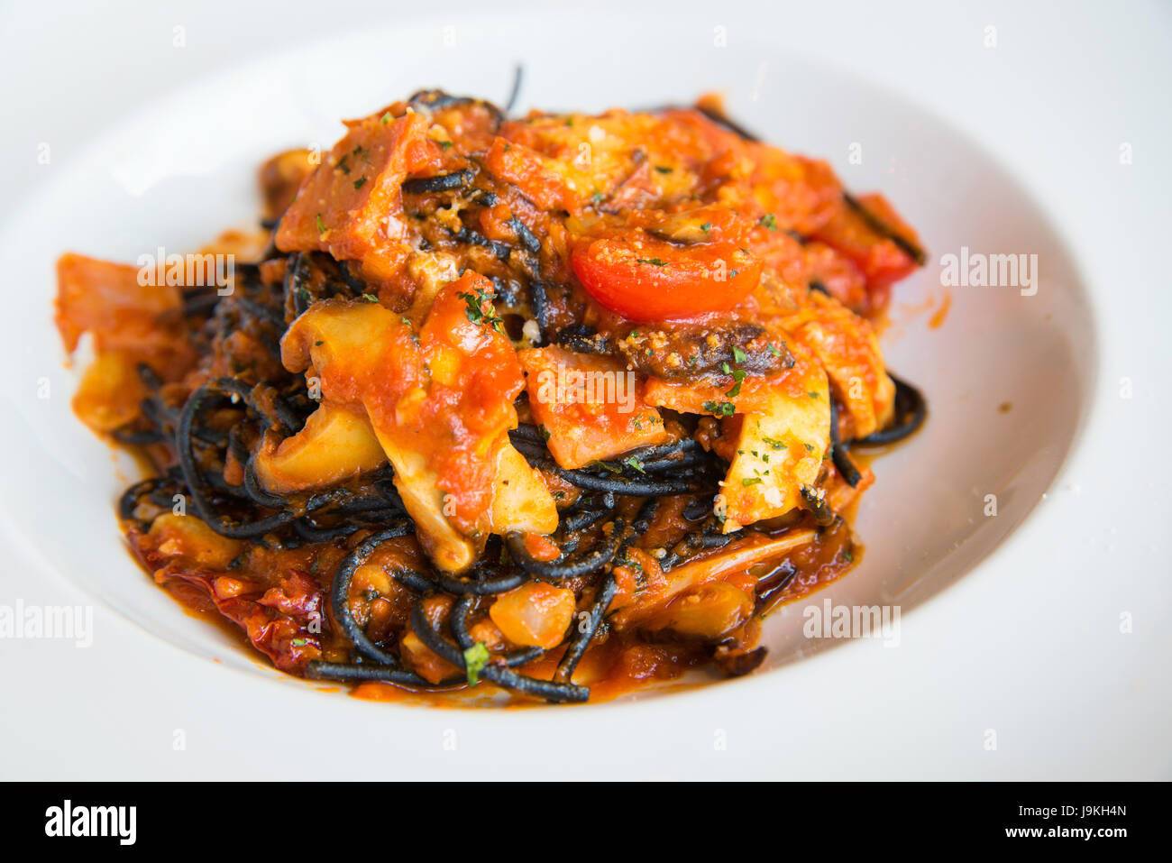 Black spaghetti sauce, chili, seafood with raw tomato in white disk. Stock Photo