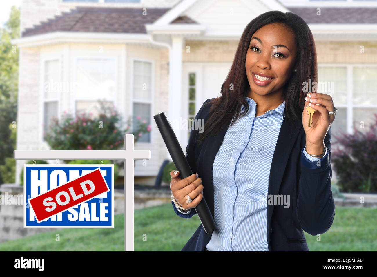 African American real estate agent holding keys in front of sold house Stock Photo
