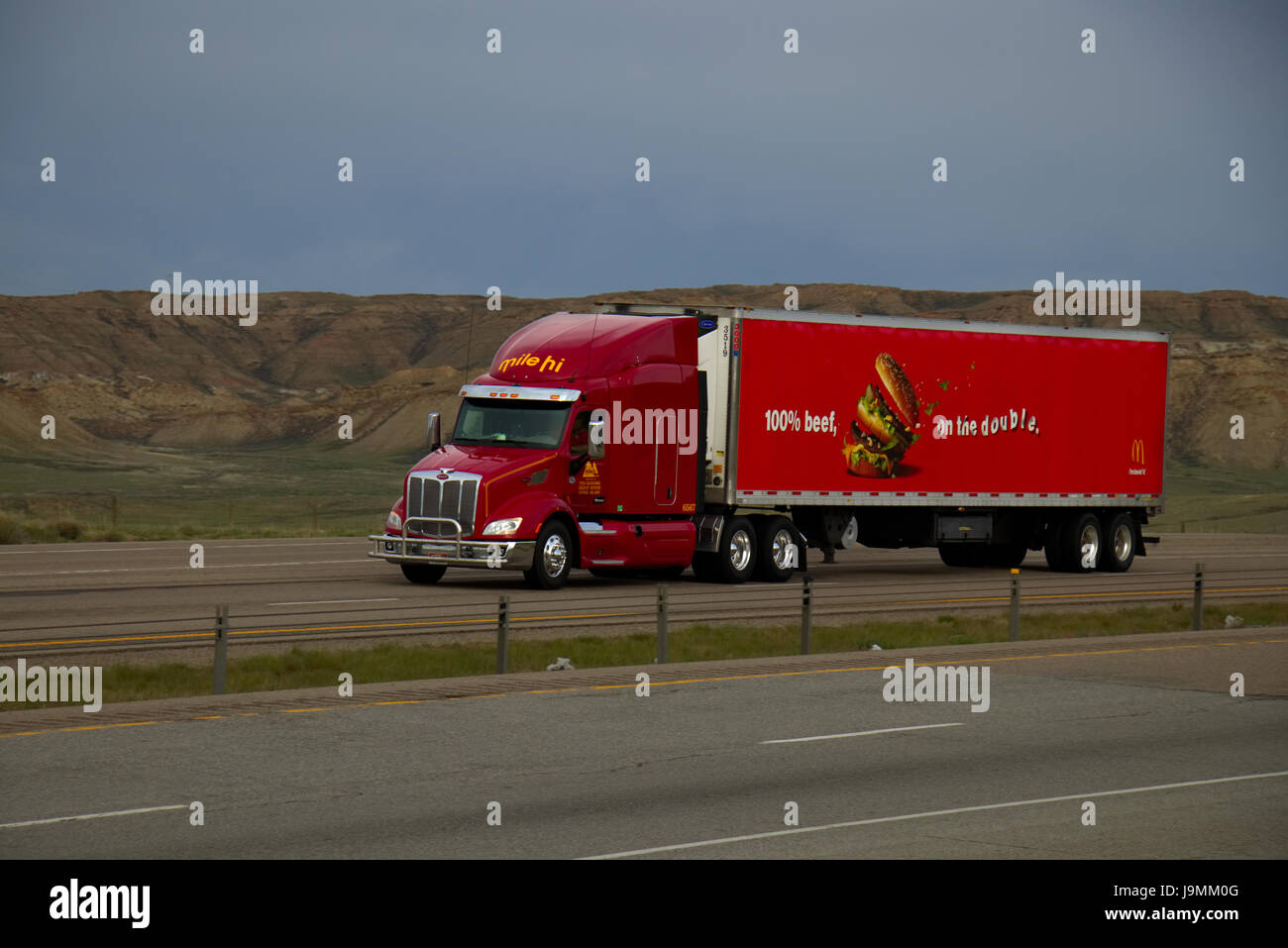 A Red 'Mile-Hi' Peterbilt Semi-Truck Pulls a Red McDonald's Food Chain Trailer along a rural US Interstate. Stock Photo
