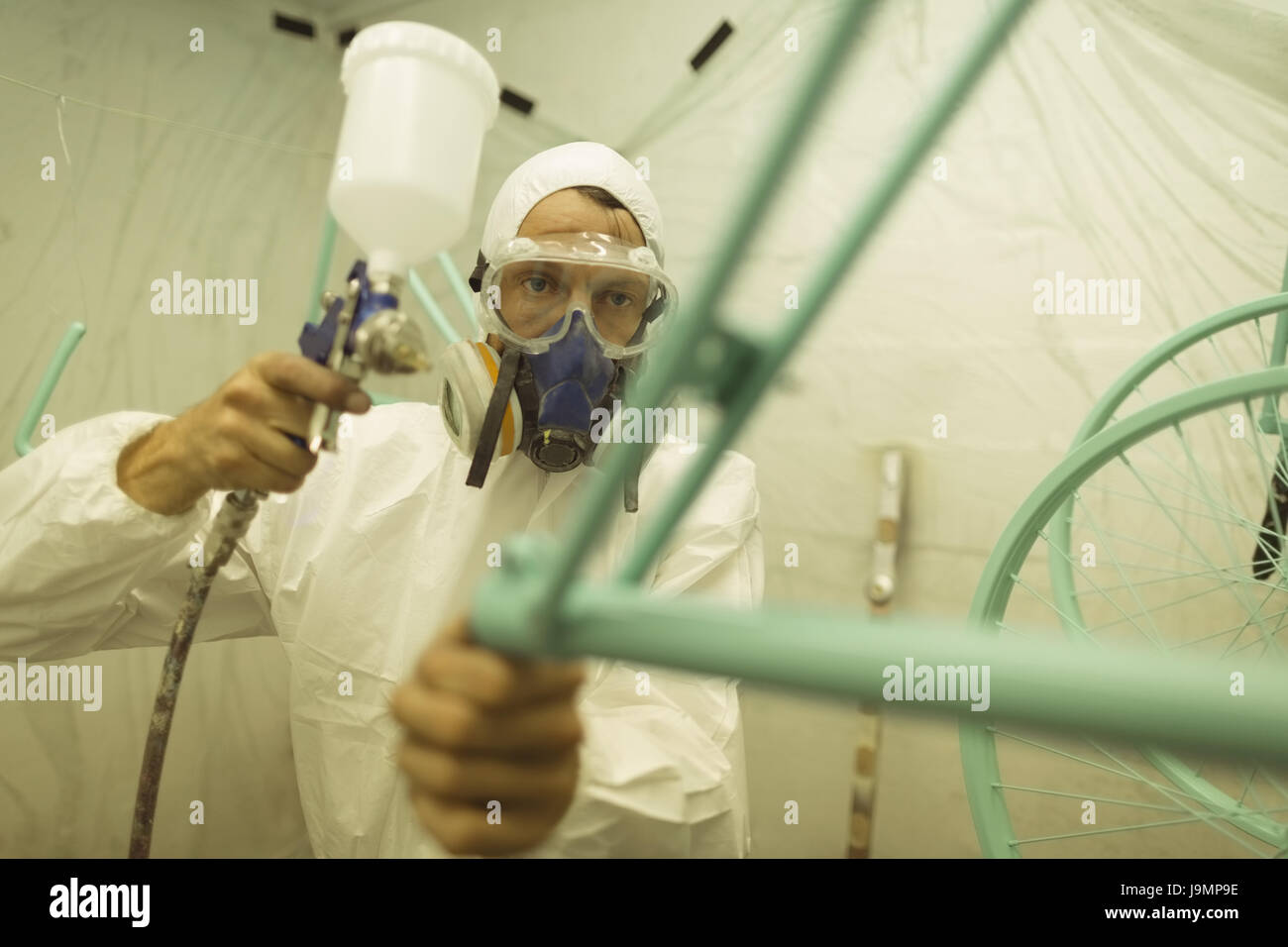 Painter painting bicycle frame through paint spray gun at
