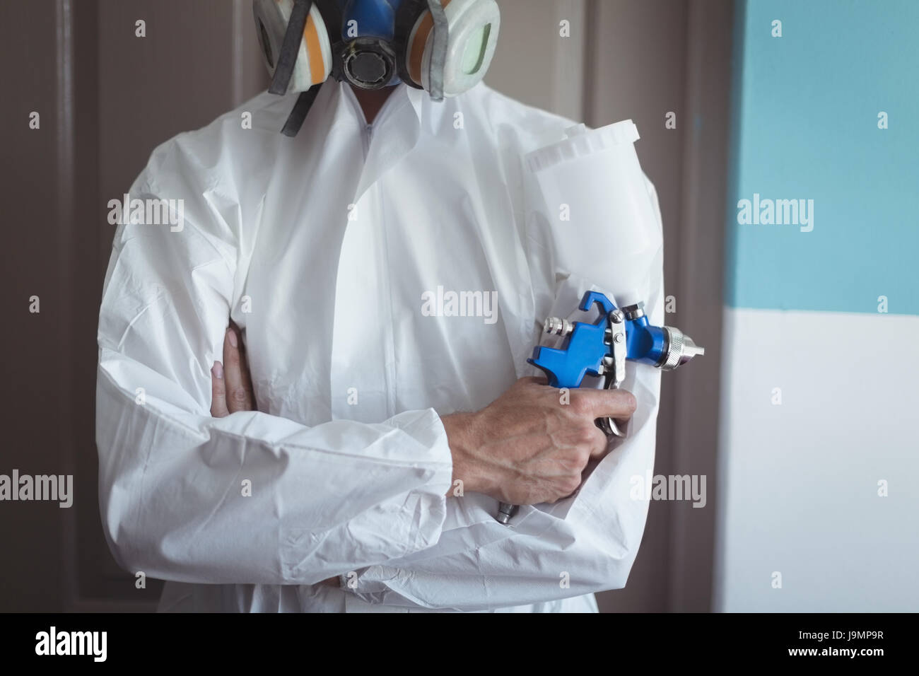 Mid section of employee holding paint spray gun while wearing gas mask at bicycle Stock