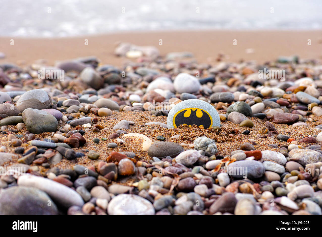 Paphos, Cyprus - November 22, 2016 Pebble with painted sign Batman lying on the sea beach with sand and stones. Stock Photo