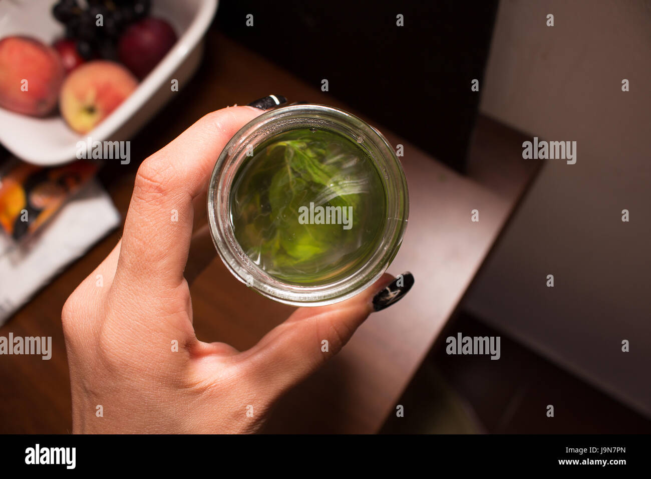 A hand serving a glass of mint tea on the background of a table with fruit. Stock Photo