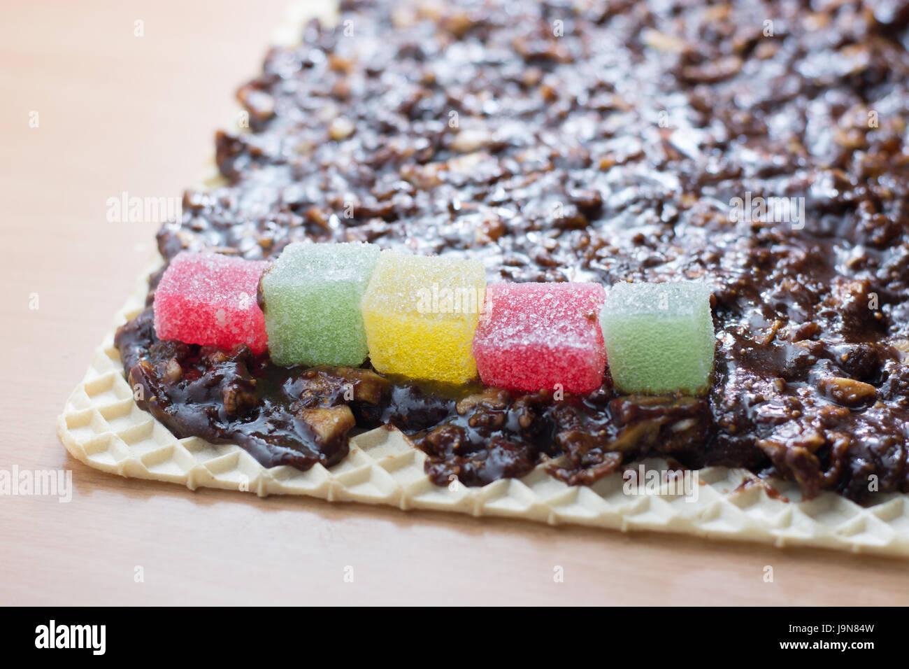 Chocolate topping with wallnuts on cake crust for rolled chocolate cake with jelly candies Stock Photo