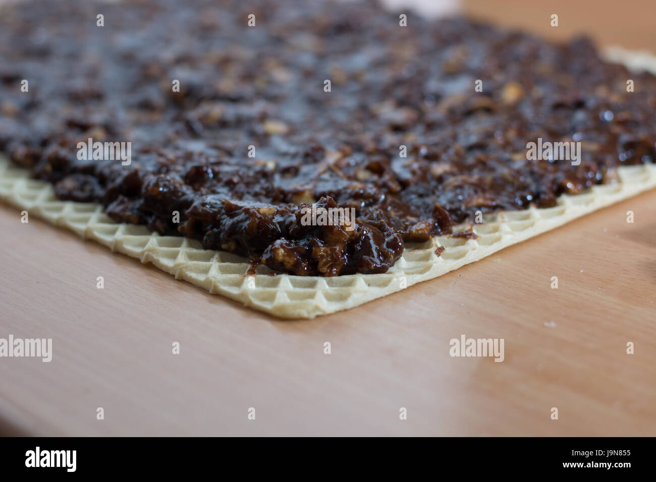 Coating chocolate topping with wallnuts on cake crust for rolled chocolate cake Stock Photo