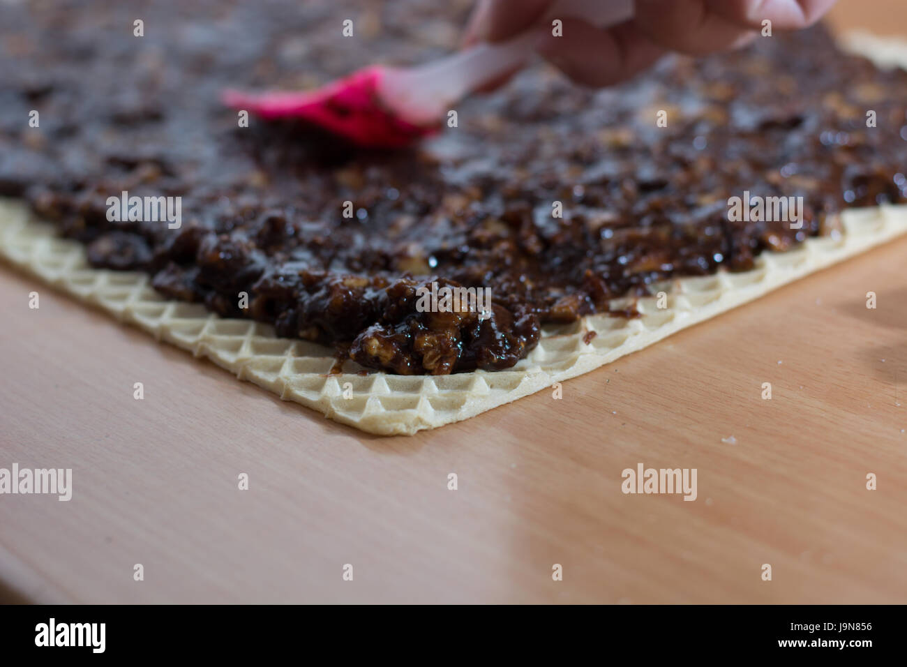 Coating chocolate topping with wallnuts on cake crust for rolled chocolate cake Stock Photo
