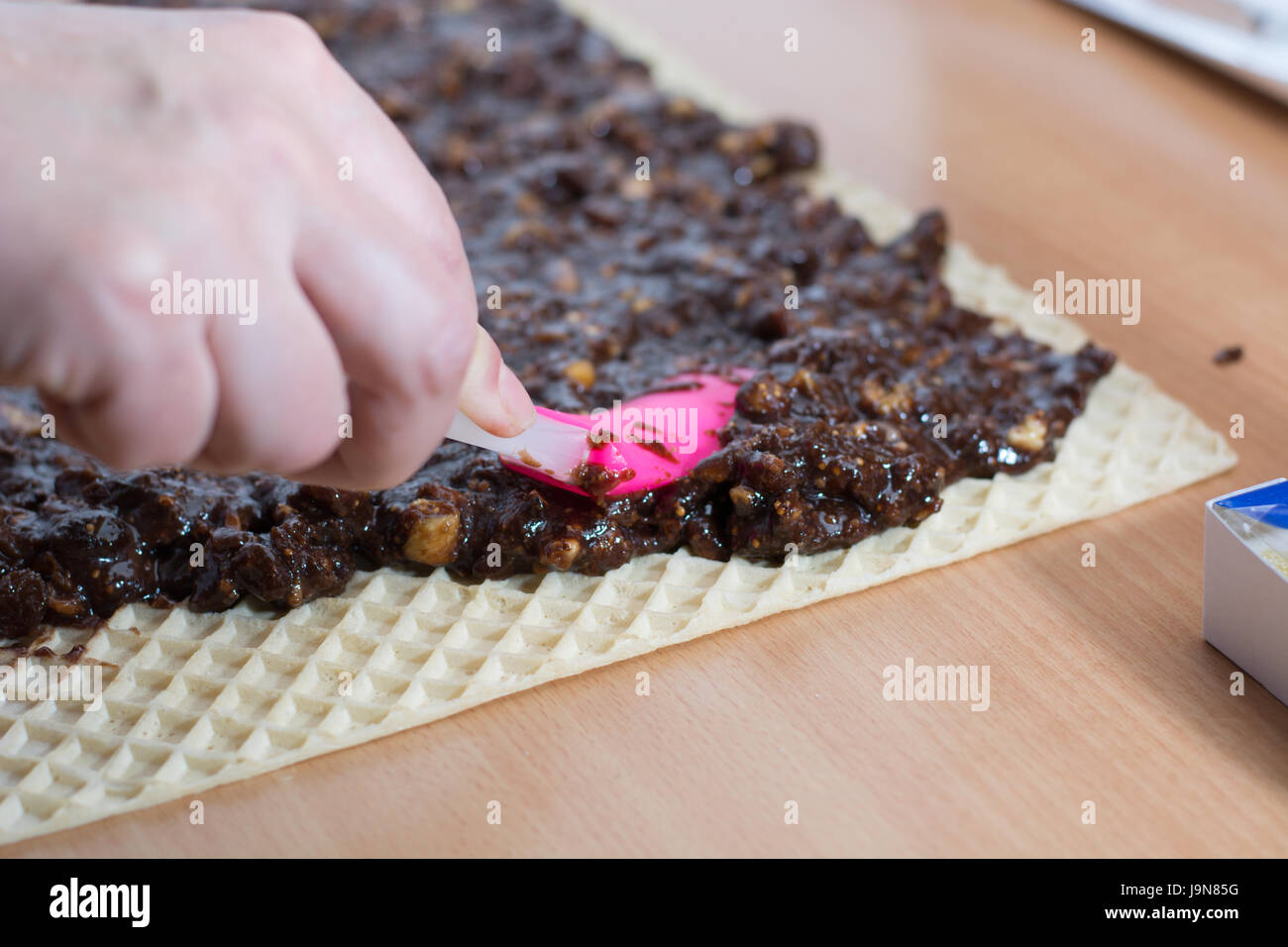 Coating chocolate topping with wallnuts on cake crust for rolled chocolate cake Stock Photo