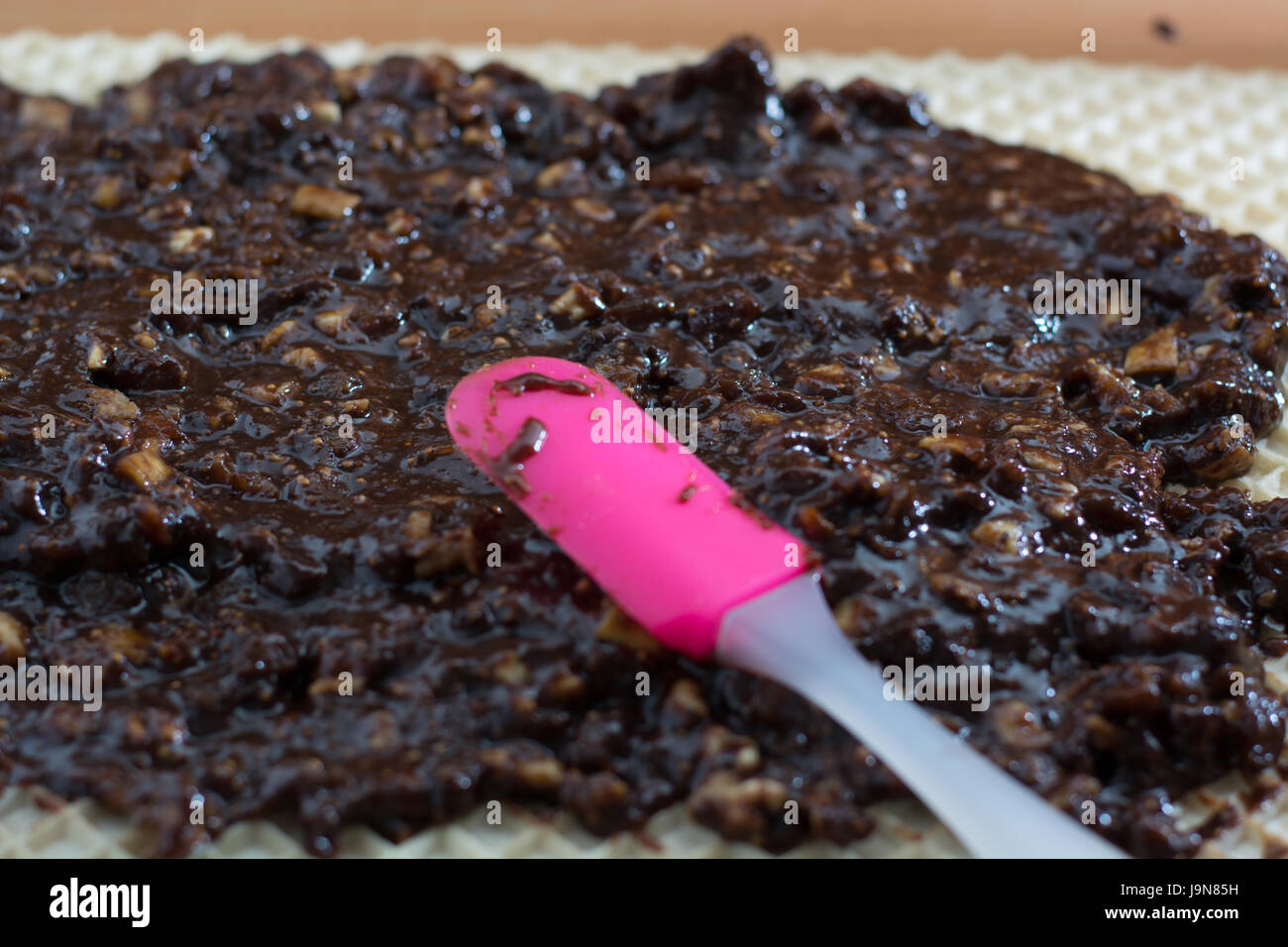 Coating chocolate topping with wallnuts on cake crust for rolled chocolate cake Stock Photo
