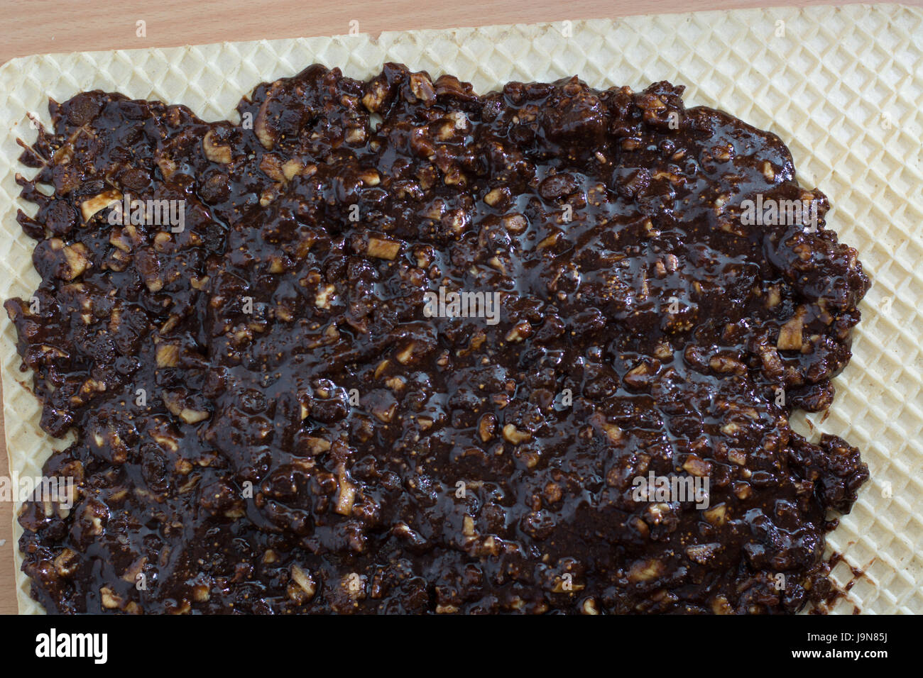 Coating chocolate topping with wallnuts on cake crust for rolled chocolate cake Stock Photo