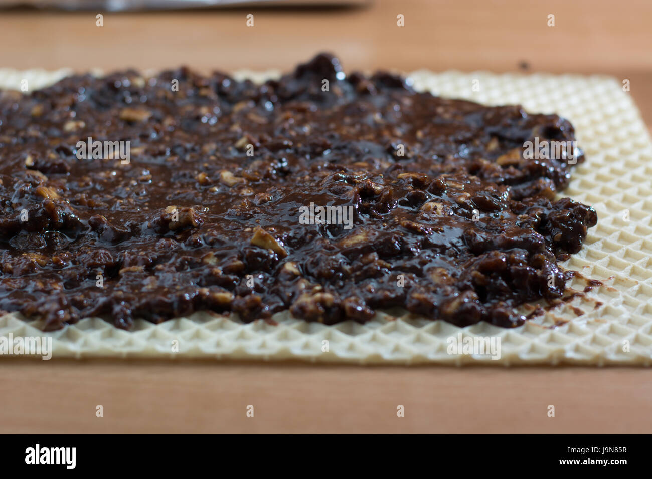 Coating chocolate topping with wallnuts on cake crust for rolled chocolate cake Stock Photo