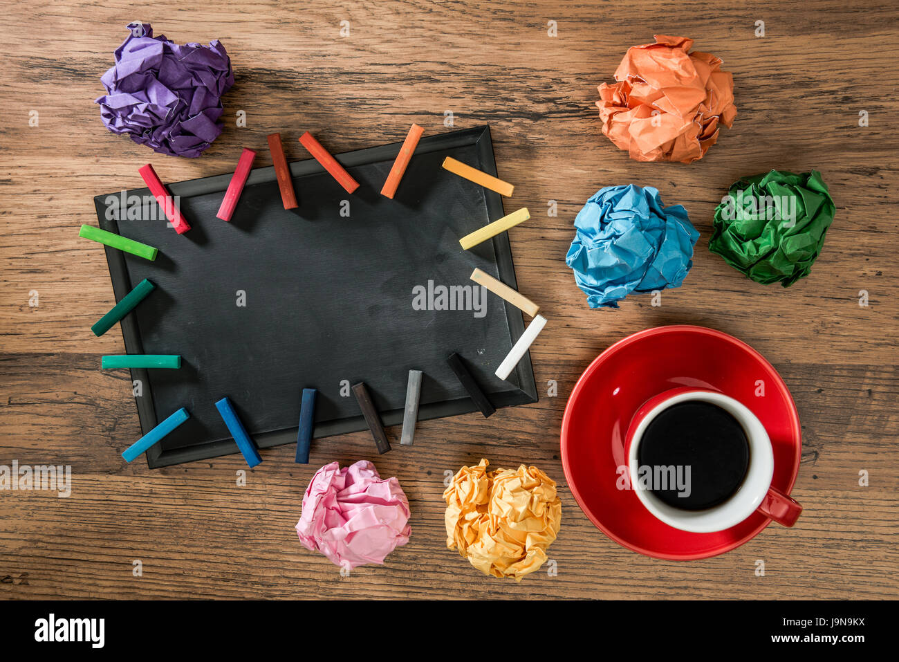 lots of paper balls with multicolor chalk on wooden desk with design inspiration for copyspace area on small blank blackboard and red cups of hot drin Stock Photo