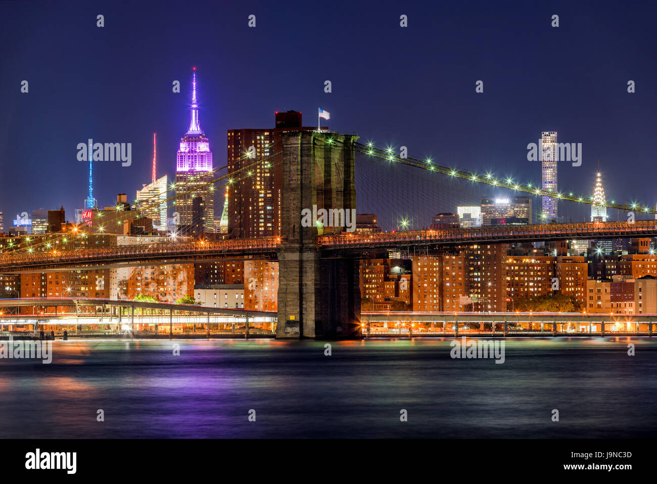 Night view of the Brooklyn Bridge and Manhattan skyscrapers with the Empire State Building lit in pink. New York City Stock Photo