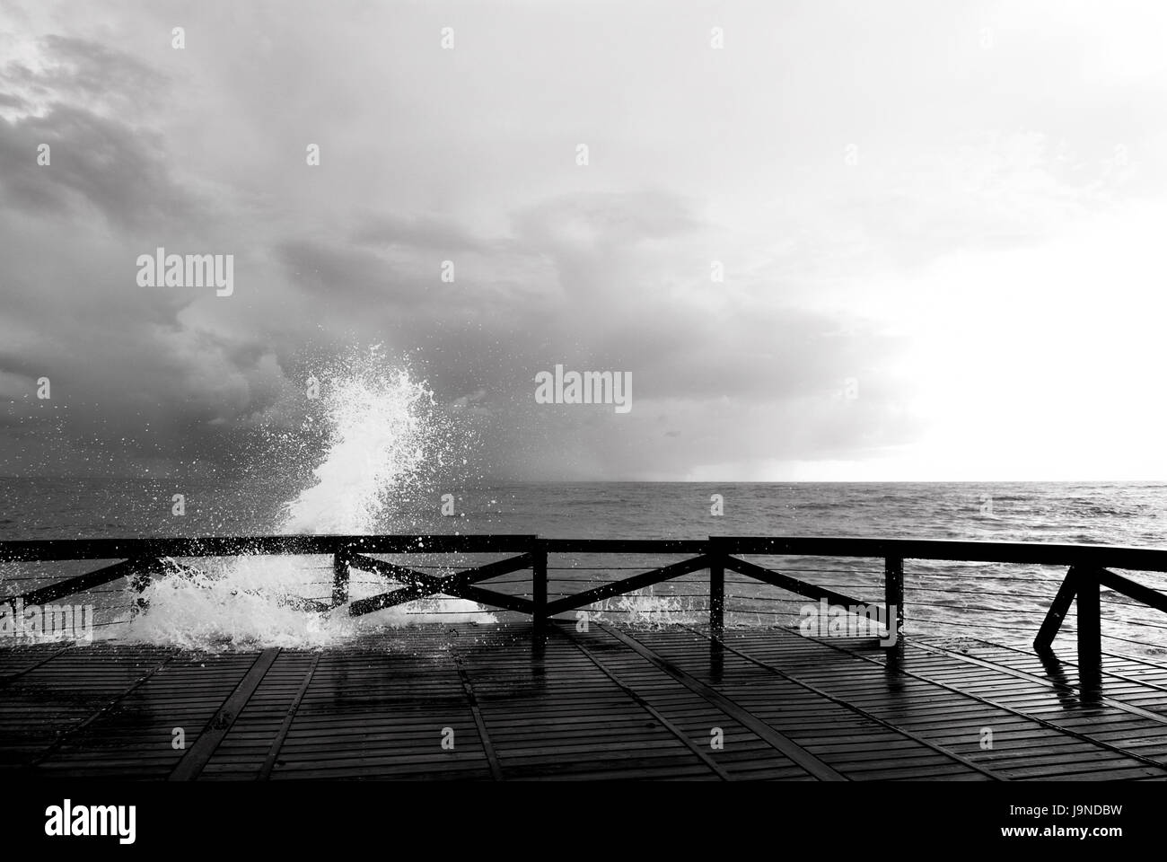 black and white photography of splash of sea on a wooden gangway Stock Photo