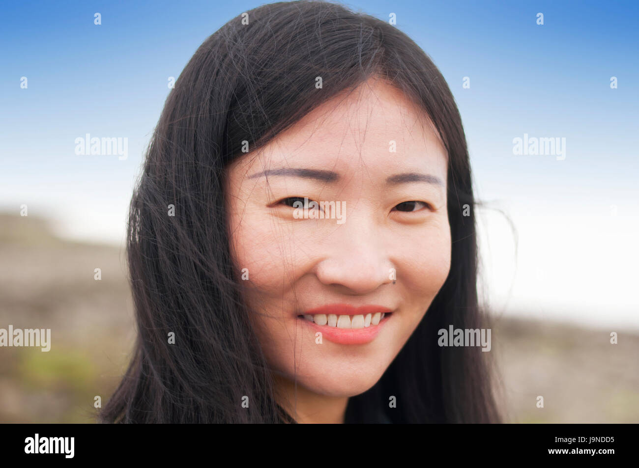 a chinese woman smiling looking at the camera with a blurred beach background. Stock Photo