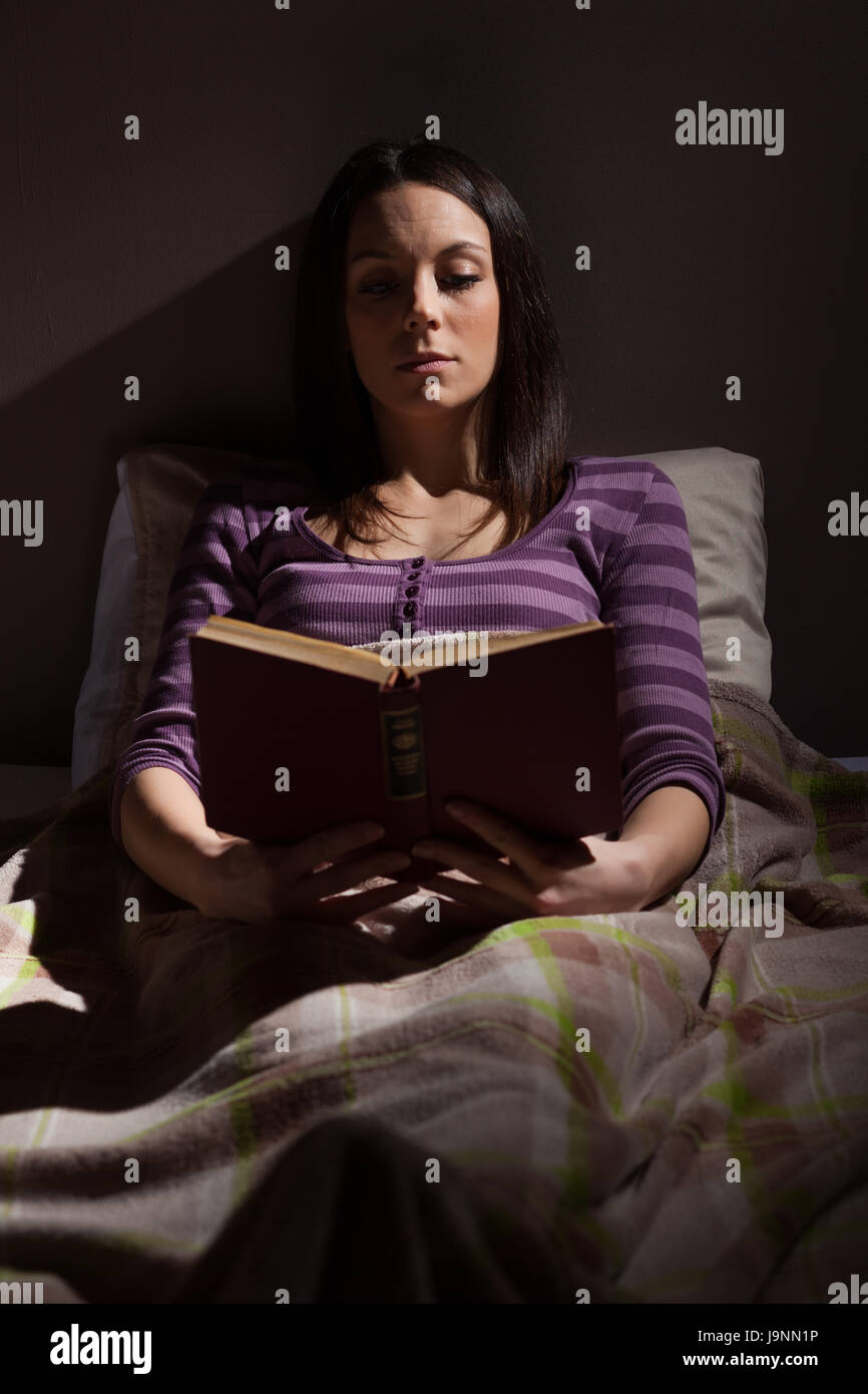 Young woman relaxing in her bed before sleep. She is reading a book Stock Photo Alamy