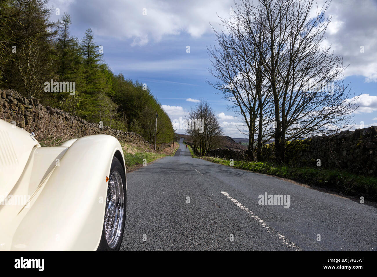 A straight tarmac road in the Yorkshire Dales photographed with the front wing of a Morgan Sports Car in the shot. Stock Photo