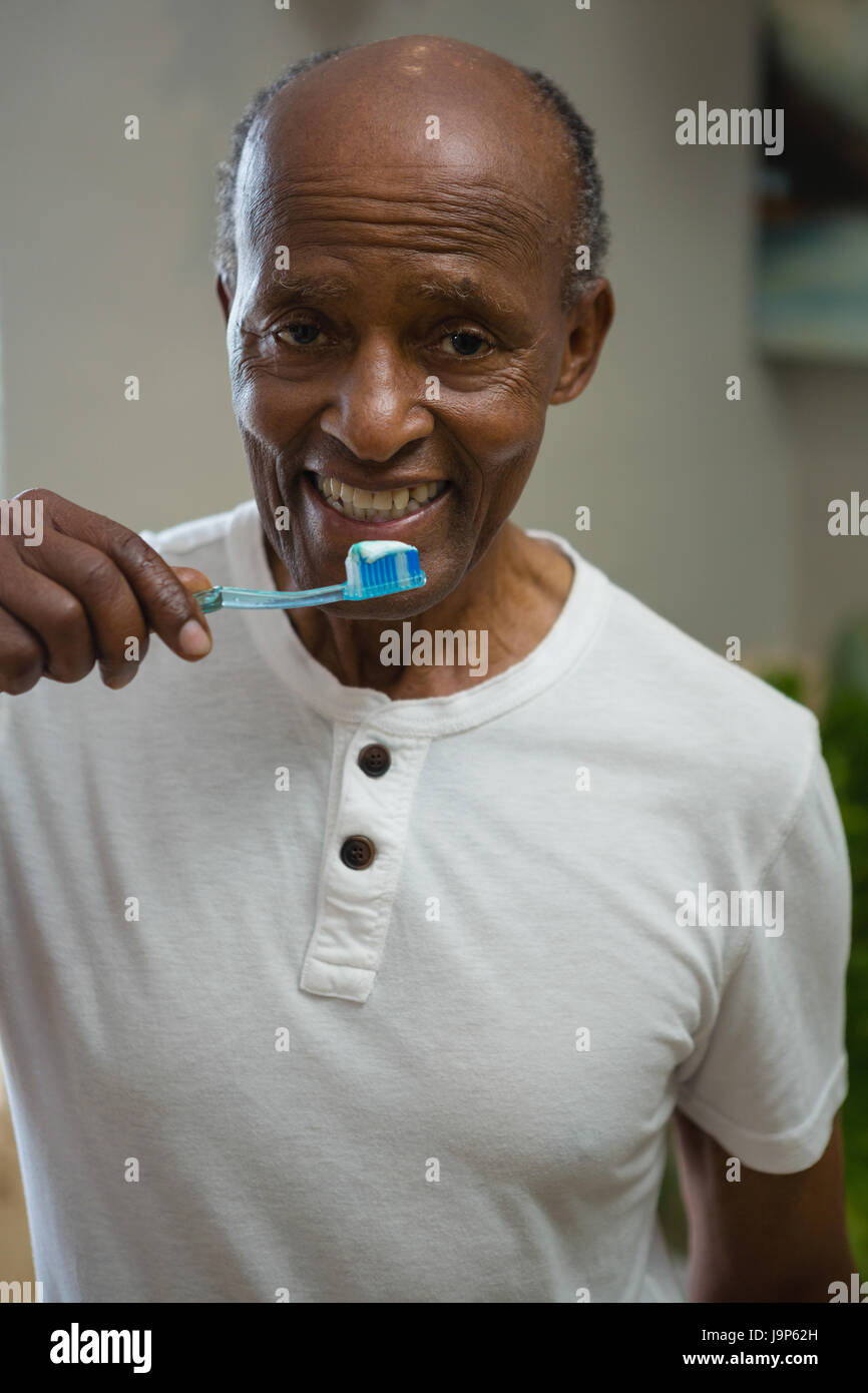 Portrait of smiling senior man brushing teeth while standing in bathroom at home Stock Photo
