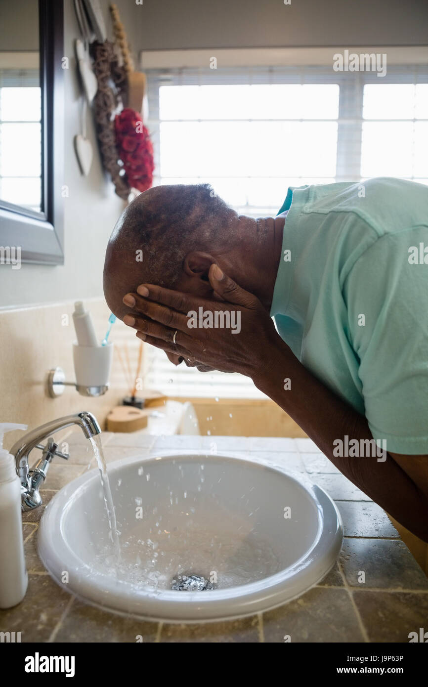Side view of senior man washing his face at sink in bathroom Stock Photo