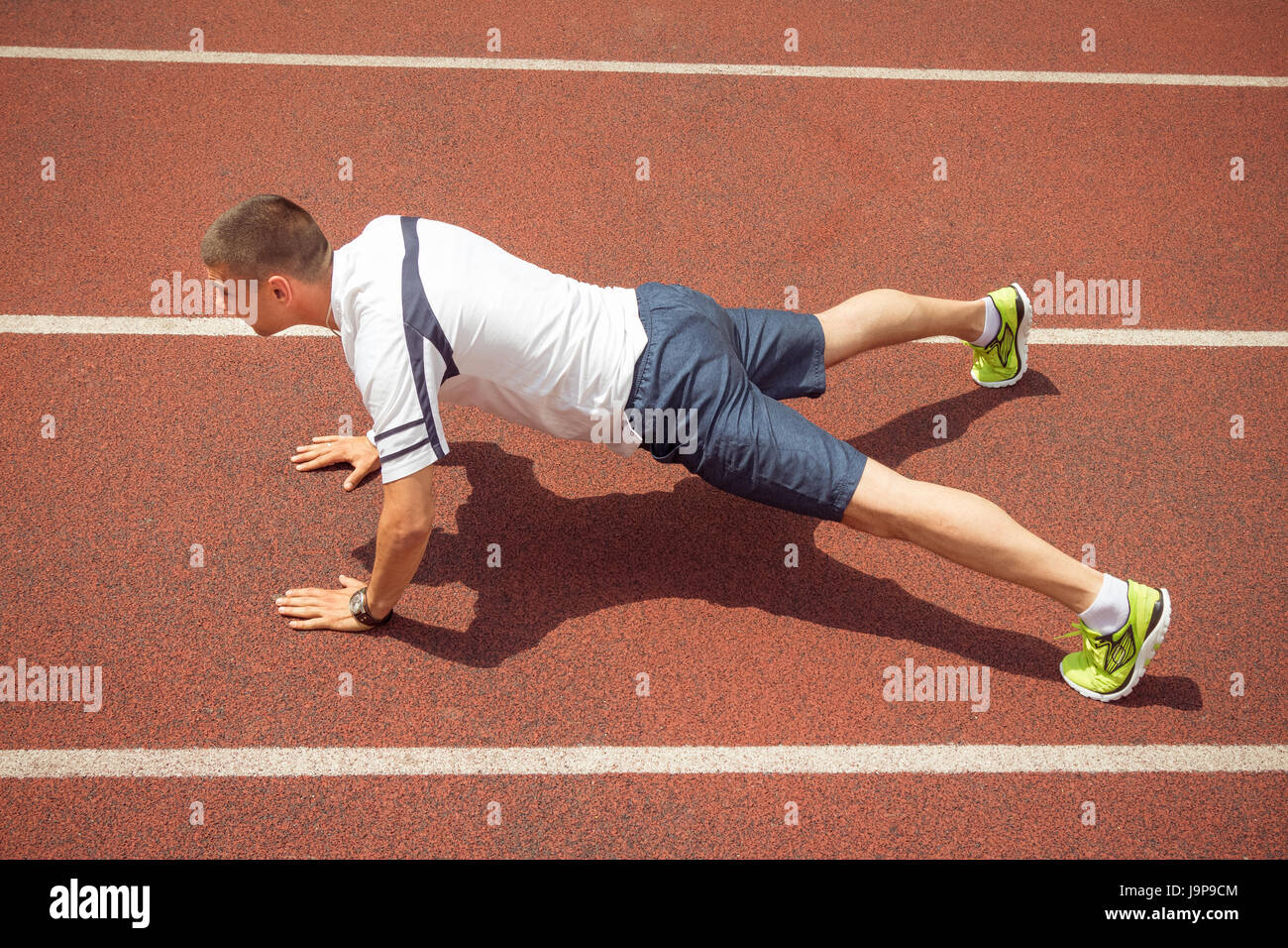 Side view of fitness man doing push ups on running track outdoors