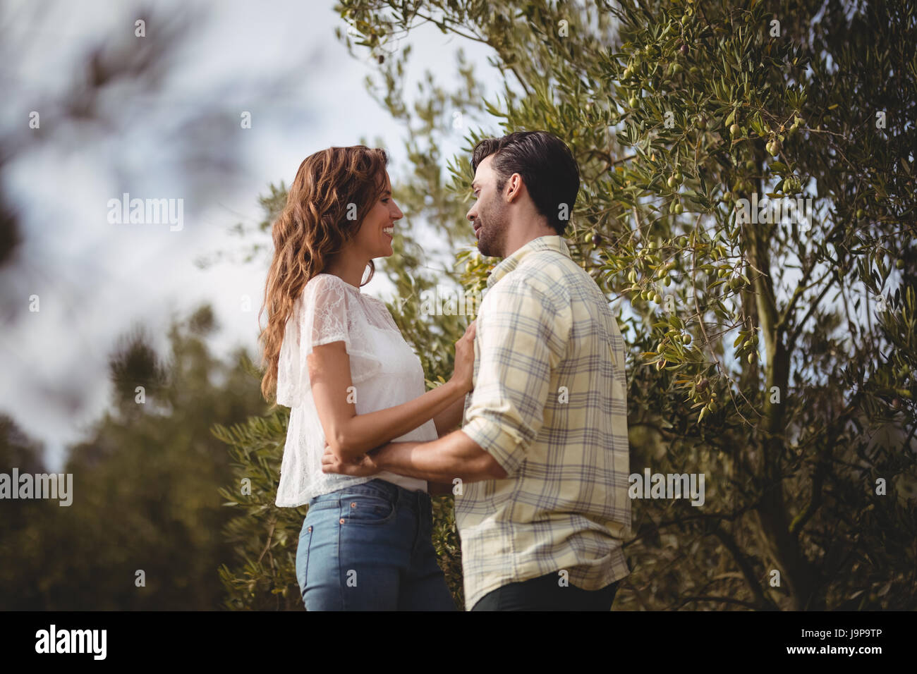 Side view of loving young couple standing by trees at farm Stock Photo ...