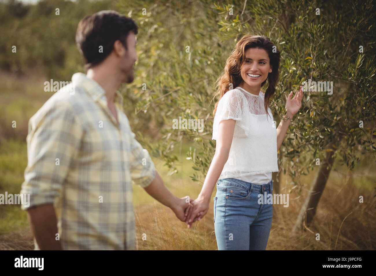 Smiling young couple standing by tree at farm Stock Photo - Alamy